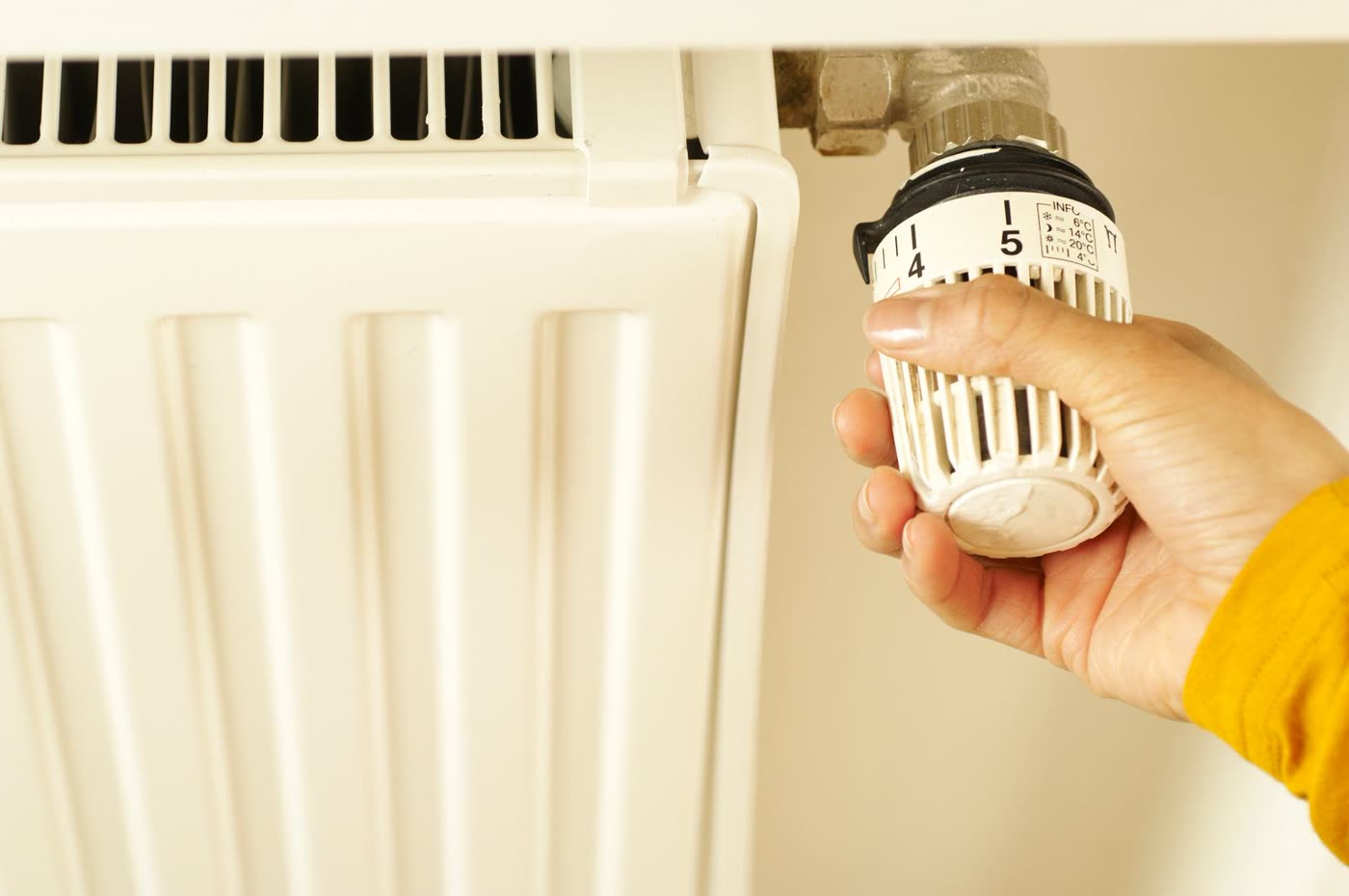 Hand dreht das Thermostat an einem Heizkörper